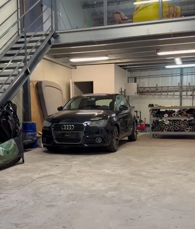 Audi A1 noire garée dans l’atelier de Chaponost, devant les rouleaux de tissu