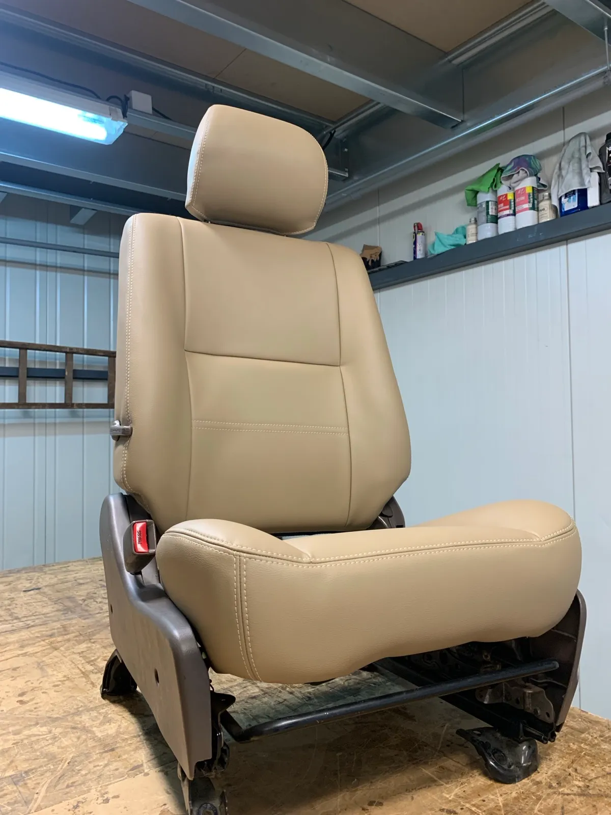 Siège avant de Toyota Land Cruiser regarni en simili beige, posé sur l’établi de l’atelier
