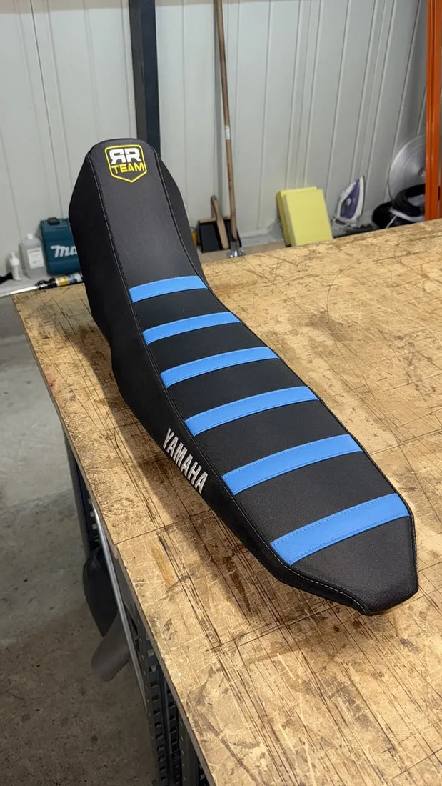 Selle de Yamaha 700 Ténéré refaite en simili noir avec bandes bleues et broderie Yamaha, posée sur l’établi